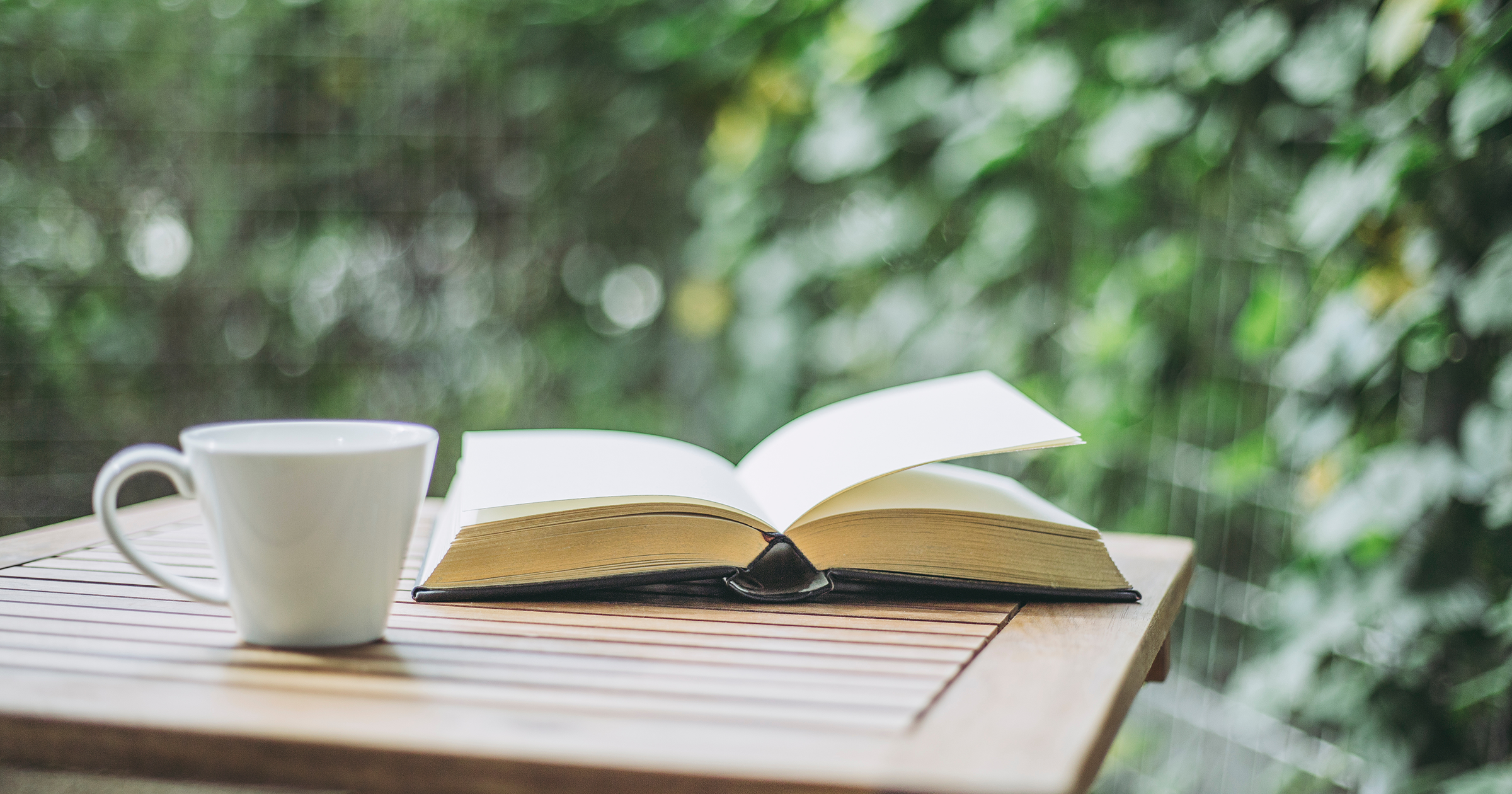 a book and hot drink sit on a wooden table in a plant lined, tech free garden space