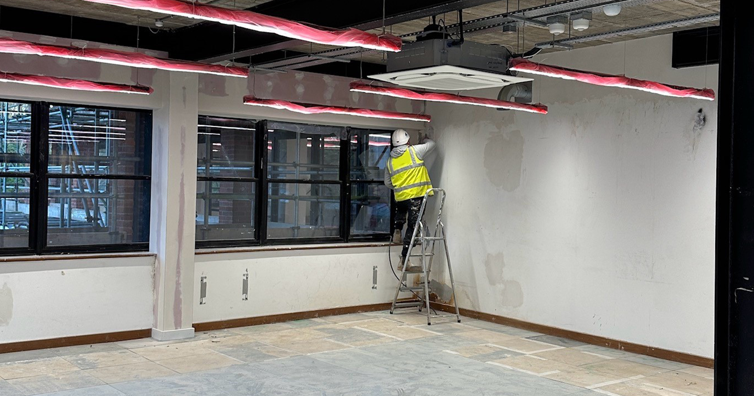 MJS Group team member up a ladder decorating in brook house wearing hard hat and hi vis jacket